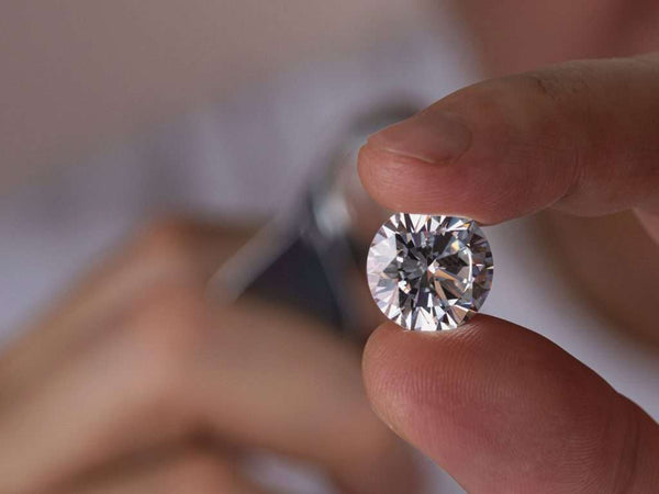 Fingers holding a round diamond up to inspect it