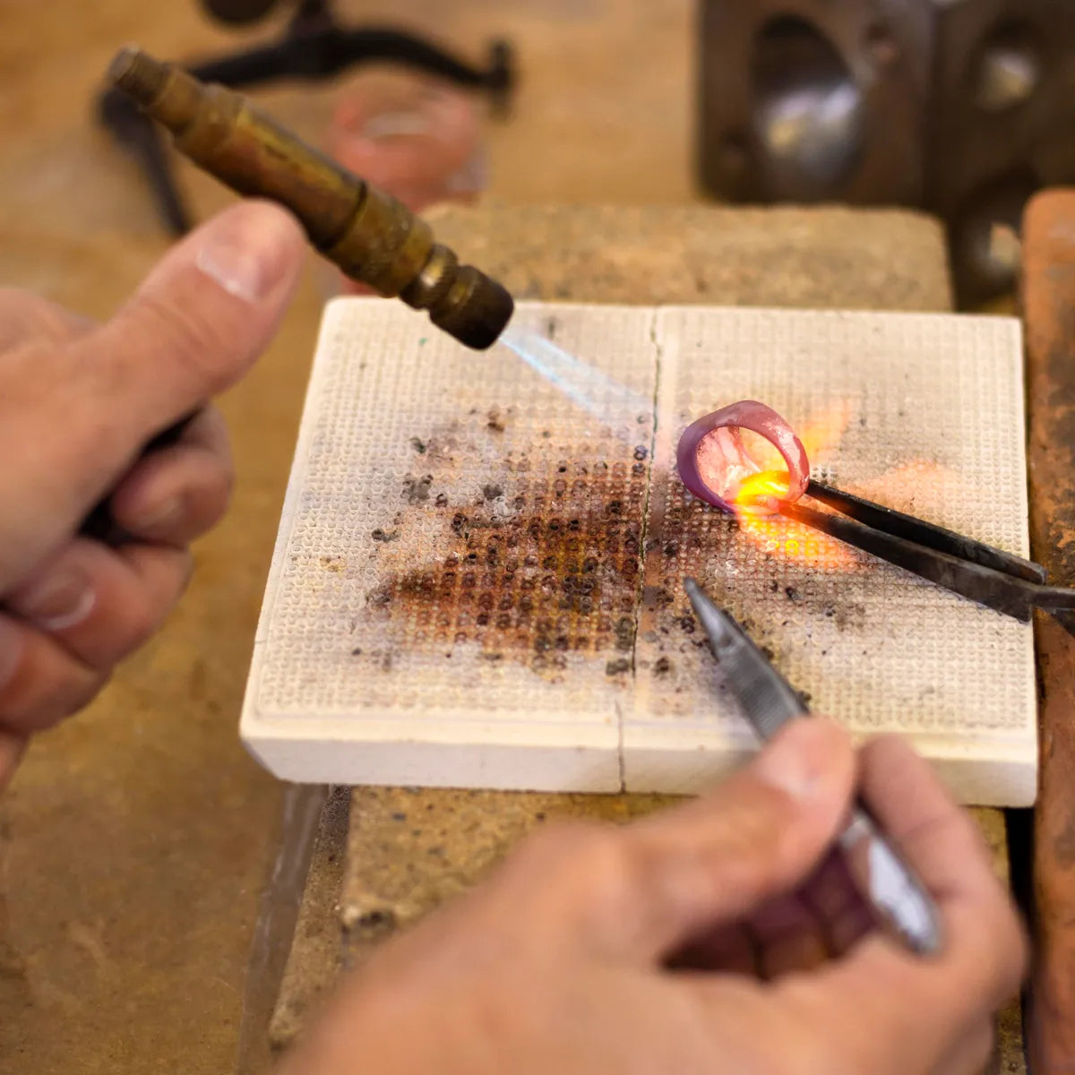 Jeweler using a torch and tweezers to repair a ring on a soldering block