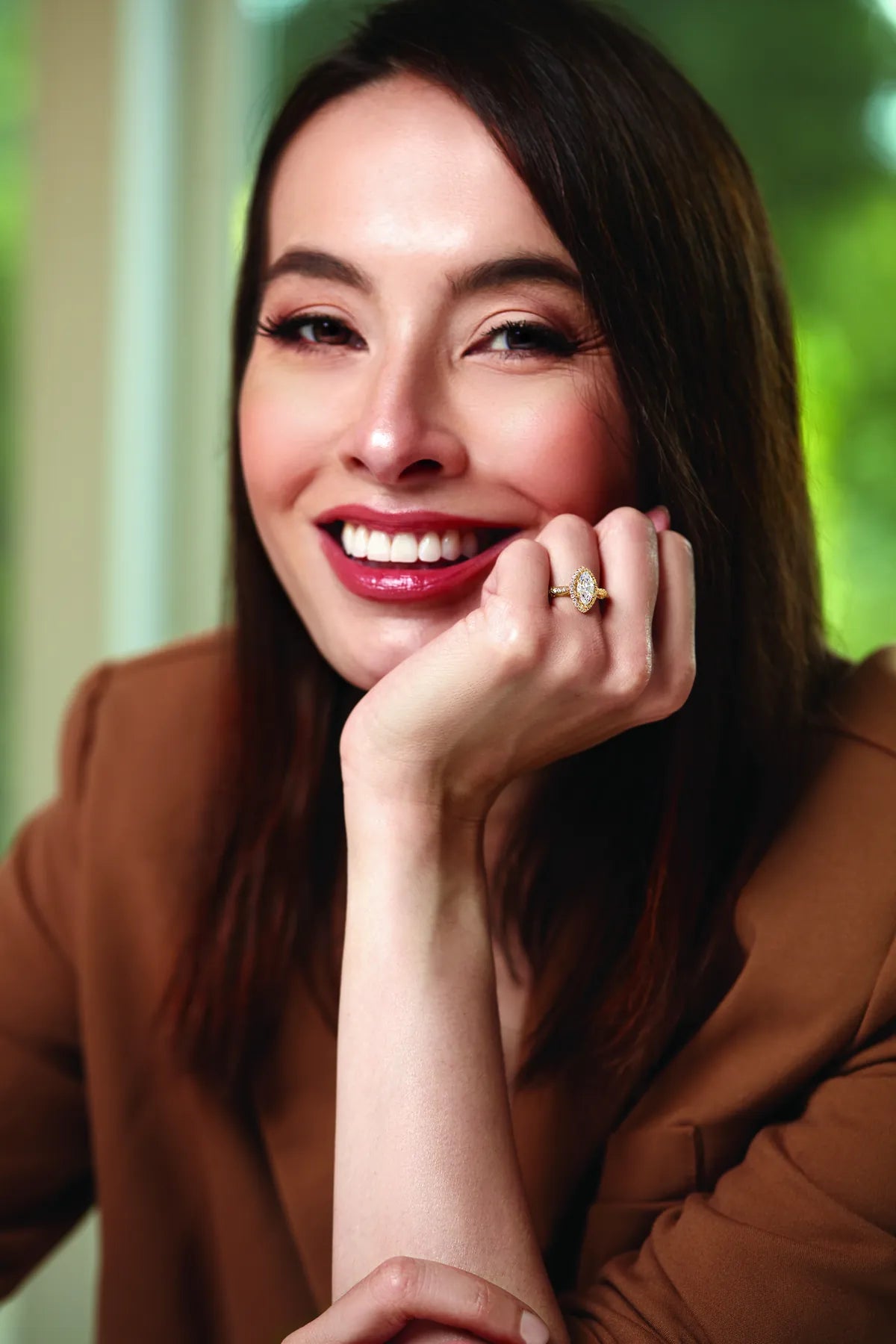 Smiling woman resting her chin on her hand, wearing a ring