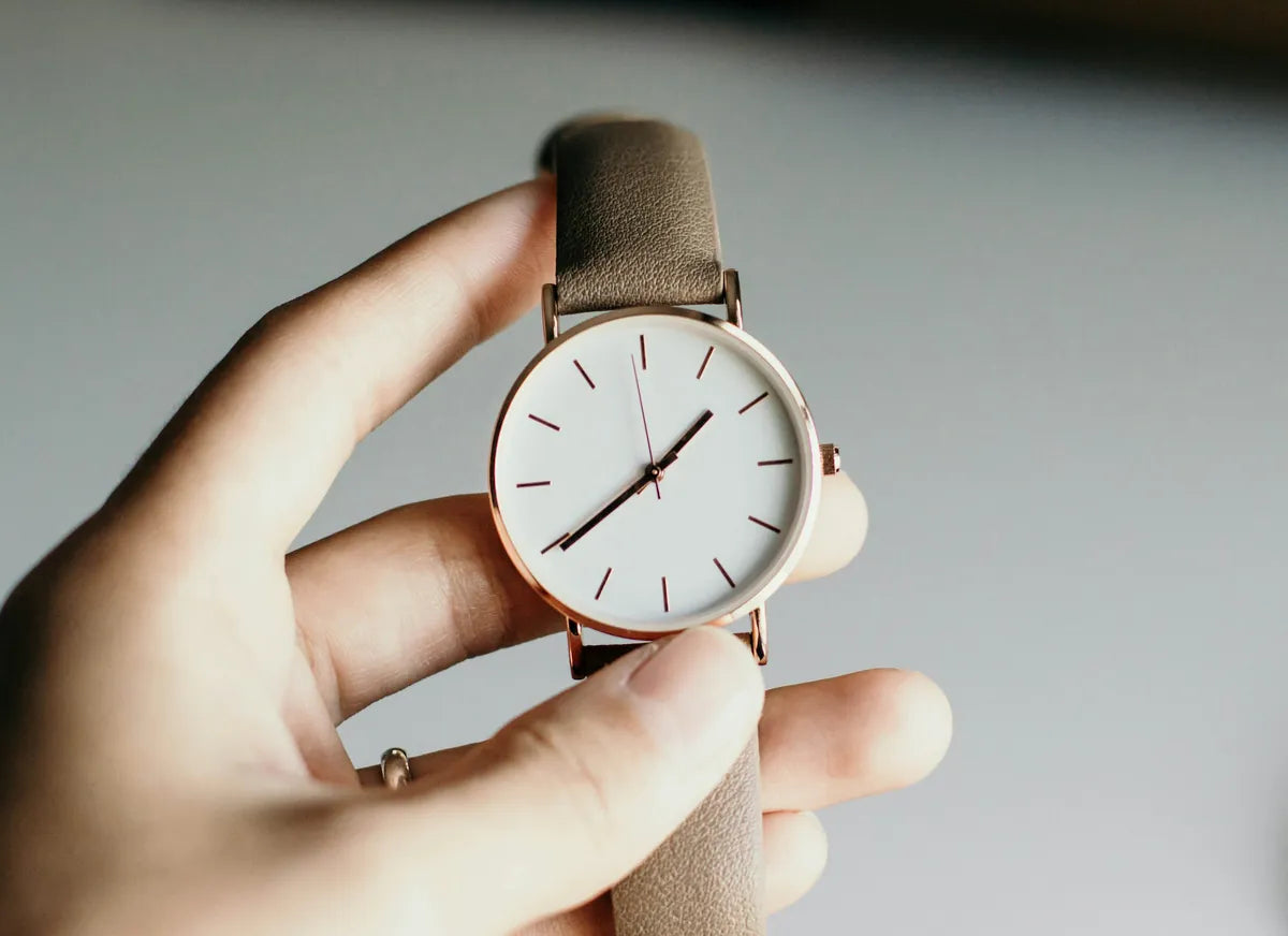 Hand holding a watch with a tan leather strap